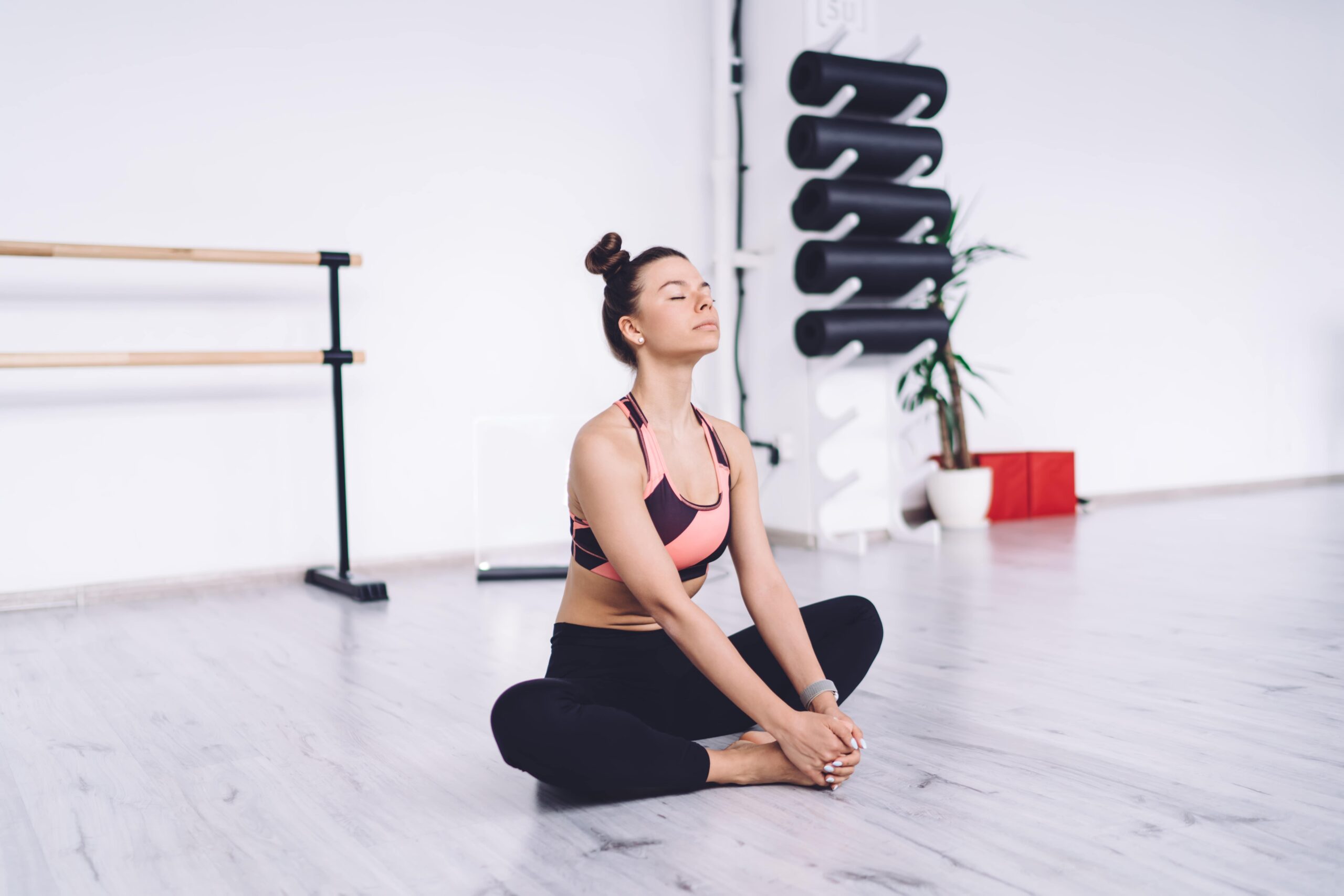 Calm relaxing fit female in sportswear with bun hairstyle sitting in butterfly position with eyes closed in bright spacious class Private suite for luxury residential treatment in California